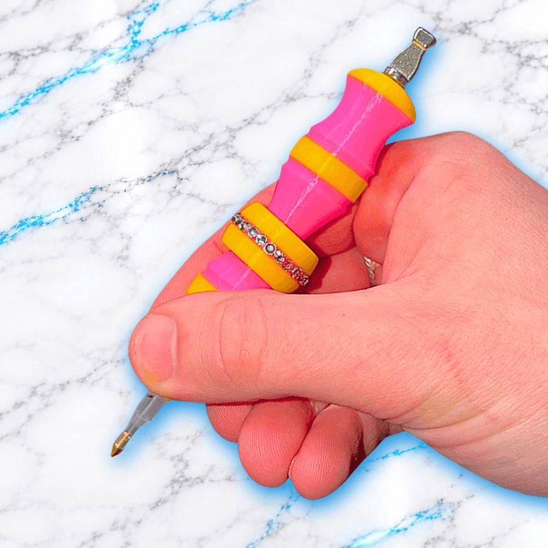 Crayon 3D GlitterPen rose et jaune tenu en main, avec poignée ergonomique, bague anti-stress centrale ornée de strass et embouts pour Diamond Painting.