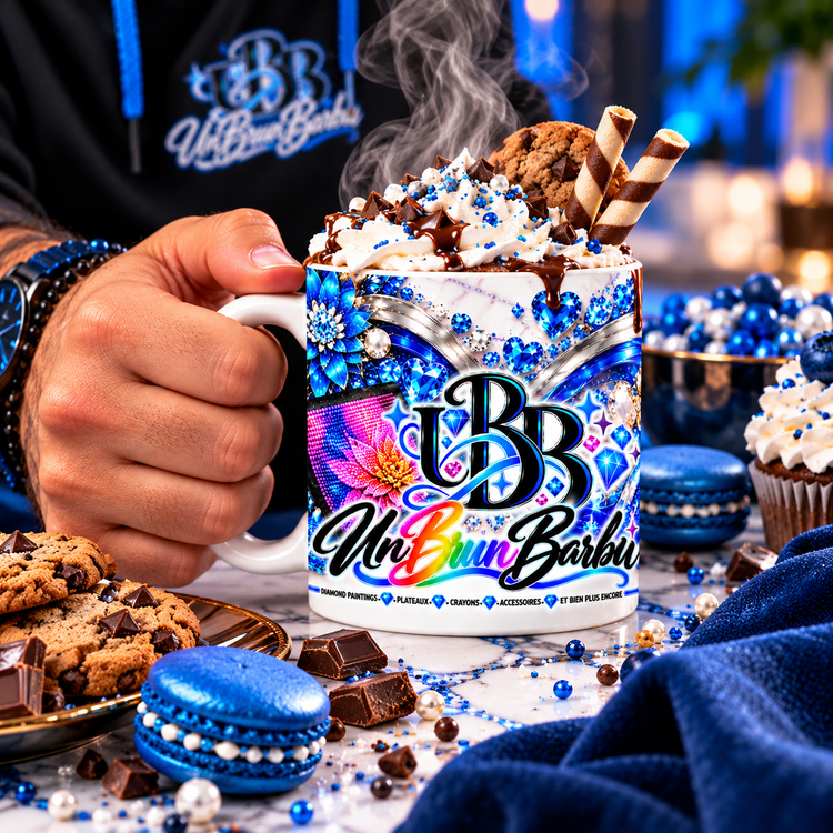 Mug Diamond Painting UBB Éclat Bleu tenu en main, garni de chantilly et de chocolat, avec biscuits et macarons bleus.