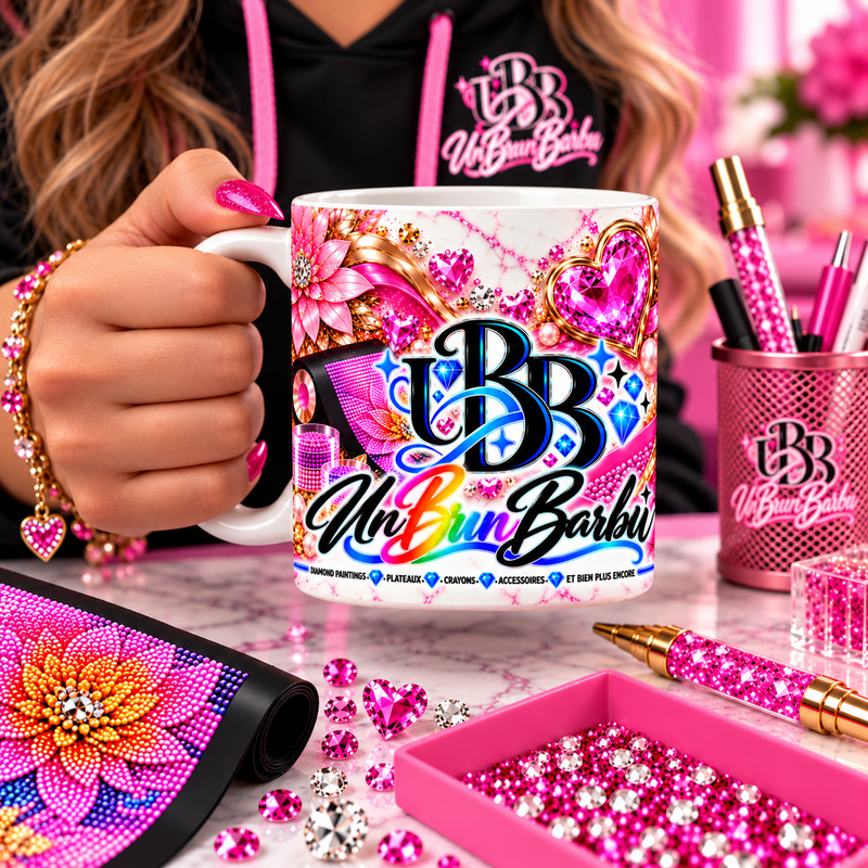 Mug Diamond Painting UBB Éclat Rose tenu en main dans un atelier créatif, avec toile fleurie, plateau rose et crayons.