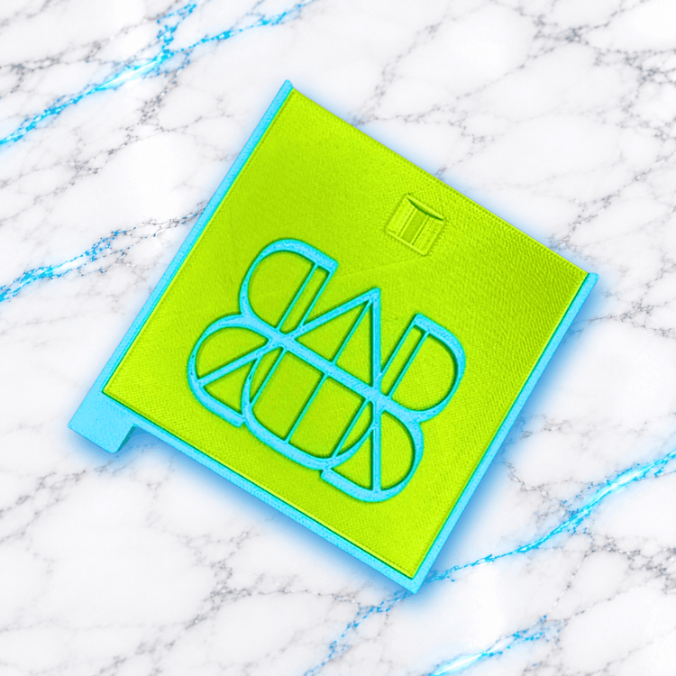 Plateau 3D Diamond Painting Le Carré Coulissable UnBrunBarbu, vue de dessus du couvercle vert anis avec bordures bleu turquoise et logo UBB en relief, présenté sur fond marbré blanc aux veines bleues.