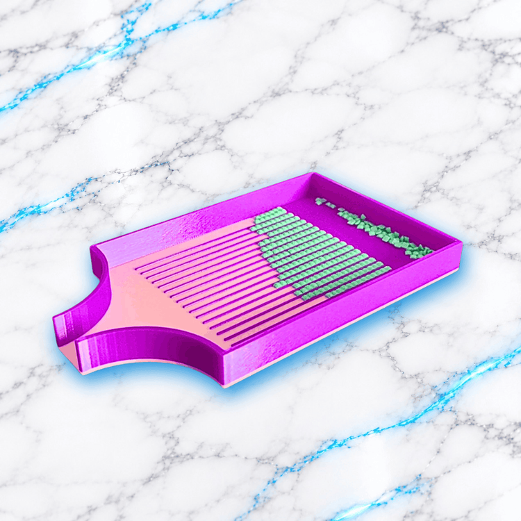 Plateau 3D Diamond Painting Le Big Indispensable UnBrunBarbu, rose et violet, avec rainures de tri alignant des diamants carrés verts et bec verseur large, photographié en perspective sur fond marbre blanc veiné de bleu.