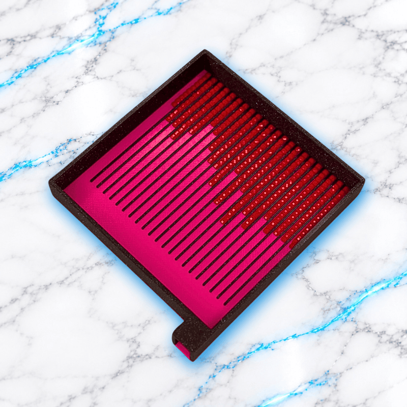 Plateau 3D Diamond Painting Le Carré Diamantable UnBrunBarbu, de forme carrée avec fond rose fuchsia, bordures noires, rainures de tri et diamants carrés rouges alignés, présenté en vue inclinée sur fond marbre blanc veiné de bleu.