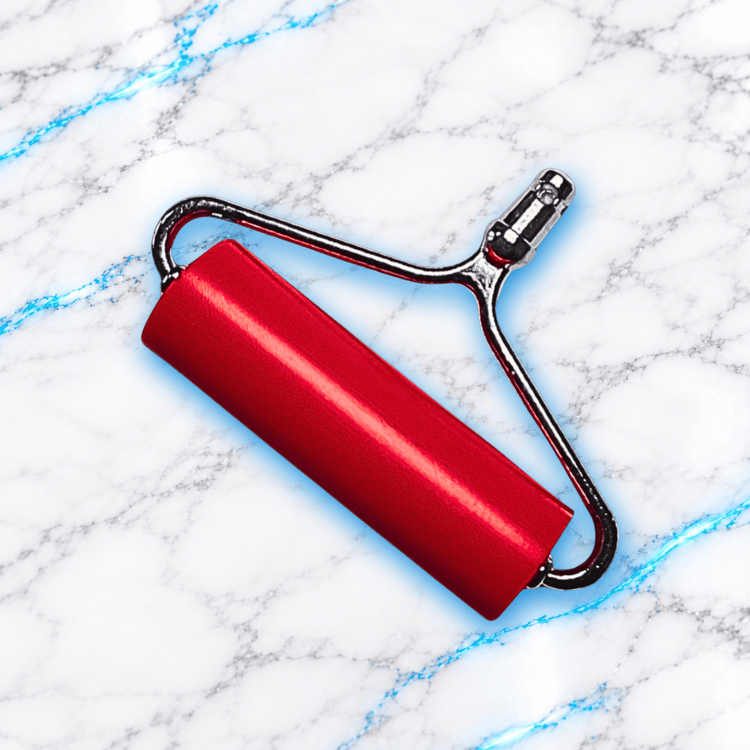 Roller Press rouge pour Diamond Painting UnBrunBarbu, rouleau de pression avec structure métallique pour bien fixer les diamants sur la toile, présenté sur fond marbre blanc veiné de bleu électrique.