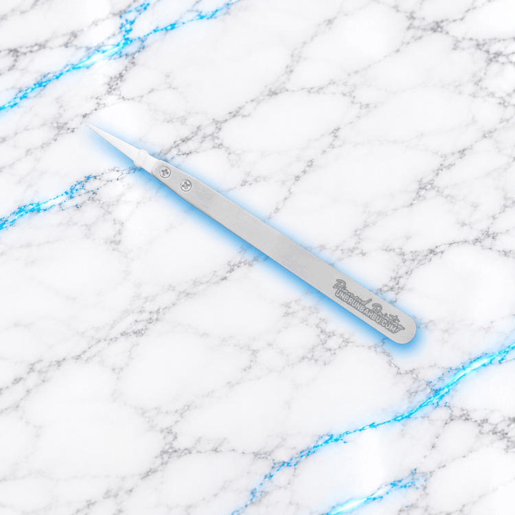 Vue détaillée d'une branche de pince Diamond Painting en métal argenté gravé UnBrunBarbu, équipée d'une pointe blanche en céramique fixée par deux vis, sur fond marbre blanc veiné de bleu.