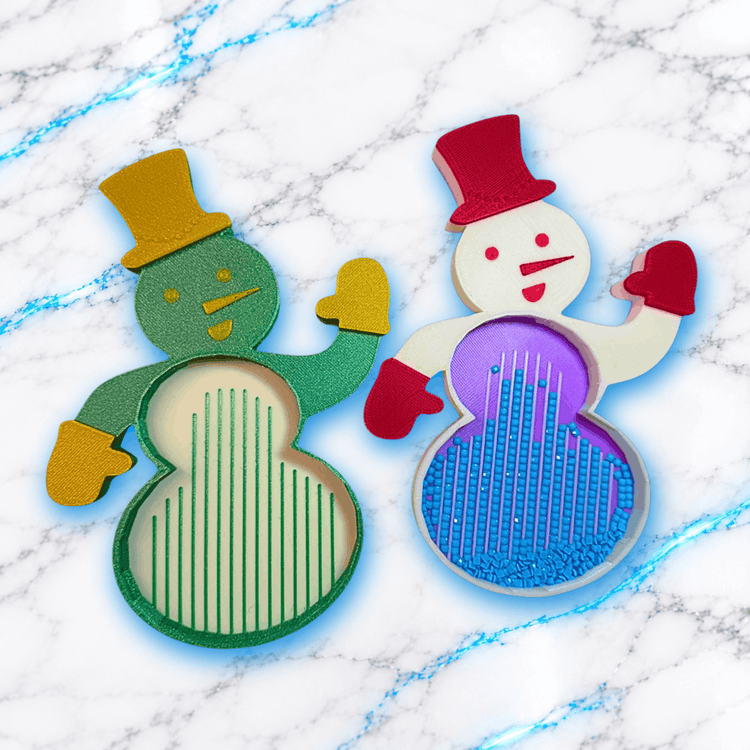 Deux plateaux 3D Diamond Painting en forme de bonhomme de neige, l'un vert avec chapeau jaune et rainures vides, l'autre blanc avec chapeau rouge, intérieur violet et diamants carrés bleus alignés, créations UnBrunBarbu.
