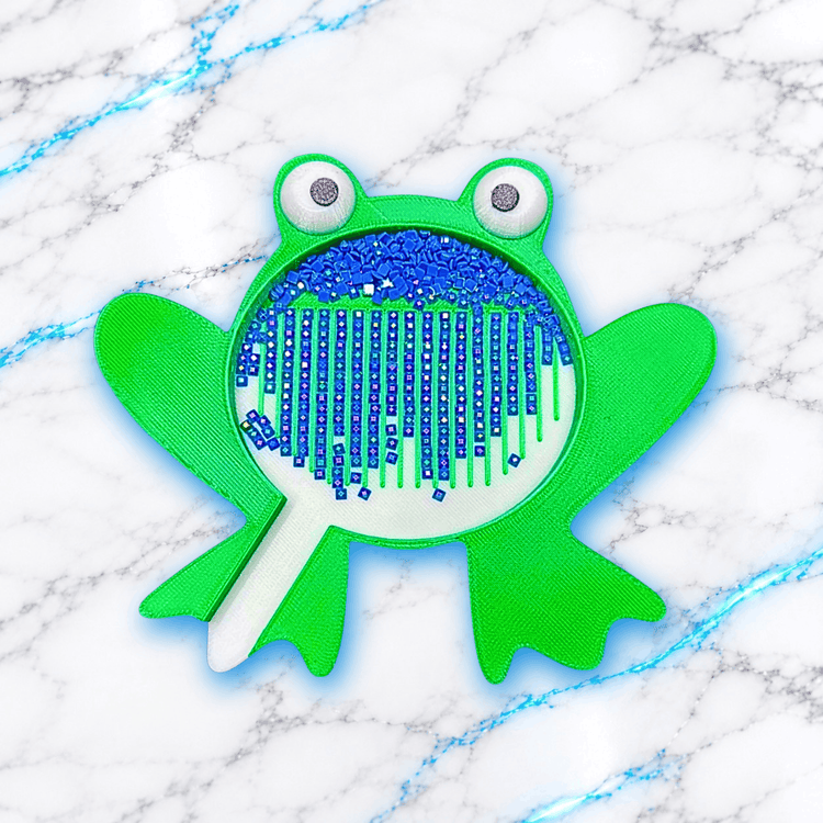 Plateau 3D Diamond Painting en forme de grenouille verte avec grands yeux, contenant des diamants carrés bleus alignés dans les rainures et une zone de récupération avec bec verseur, création UnBrunBarbu.