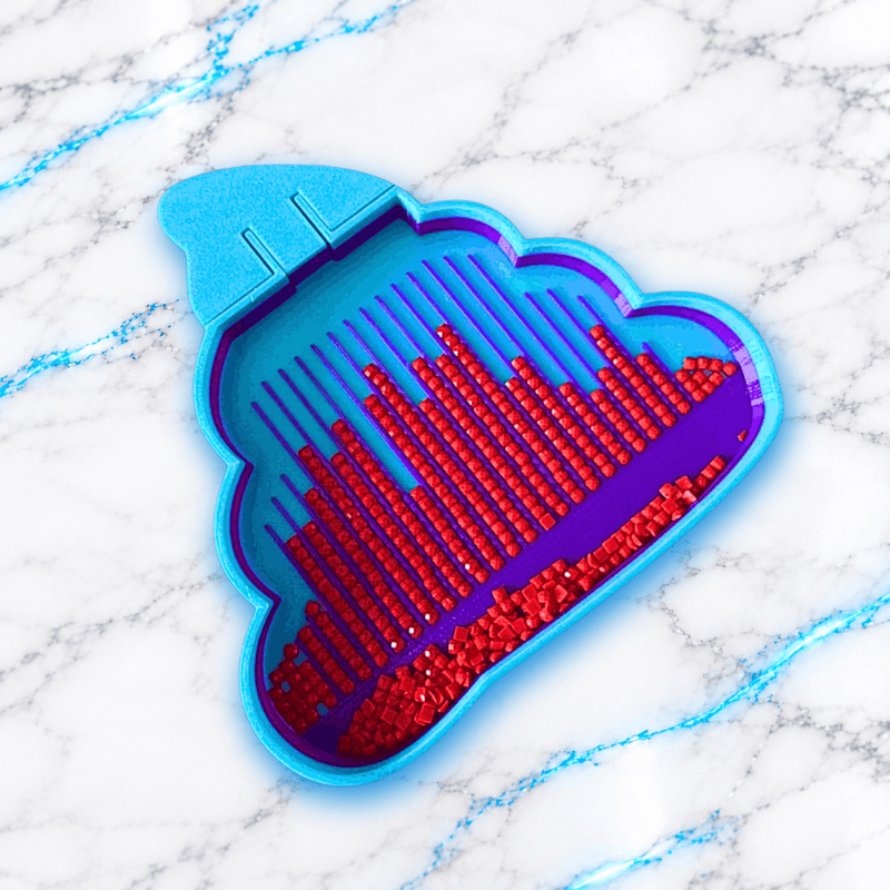 Vue de dessus du plateau 3D Diamond Painting La Crotte UnBrunBarbu, en forme de crotte stylisée bleu turquoise, avec rainures violettes remplies de diamants carrés rouges et compartiment de récupération, sur fond marbré blanc aux veines bleues.