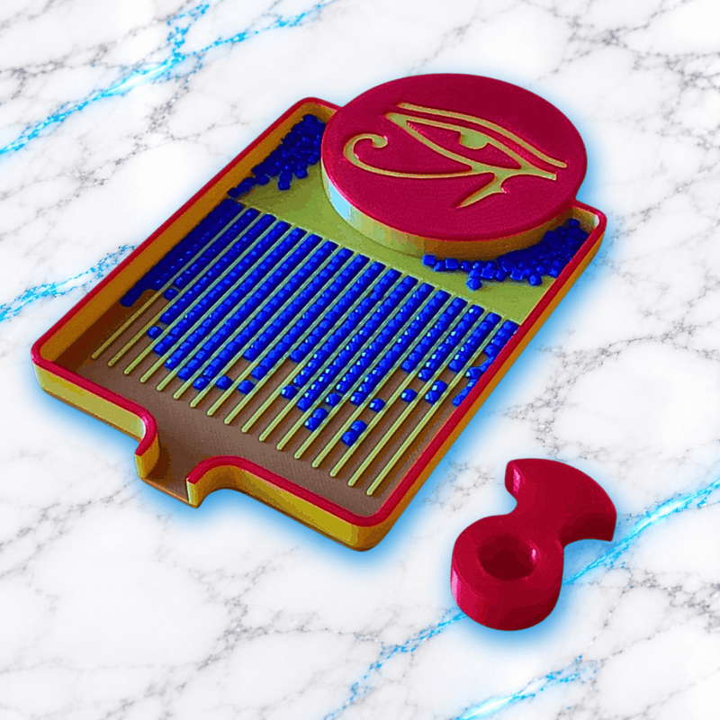 Vue rapprochée du plateau 3D Diamond Painting Symbole Égyptien UnBrunBarbu, avec médaillon rose orné de l’œil d’Horus doré, rainures de tri remplies de diamants carrés bleus et pièce amovible rose, sur fond marbré blanc et bleu.