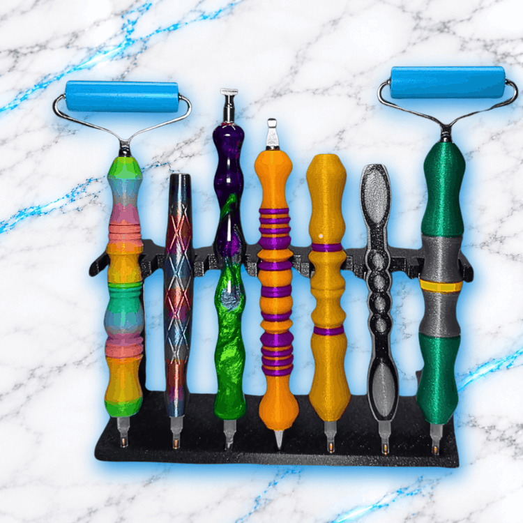 Support de rangement noir pour crayons Diamond Painting UnBrunBarbu, présenté avec sept crayons colorés et deux rouleaux de pression bleus, organisateur d'accessoires de broderie diamant sur fond marbre blanc veiné de bleu électrique.